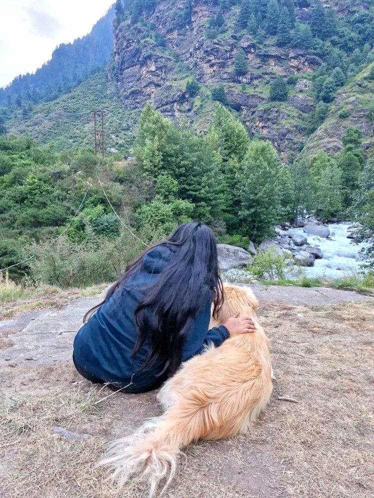 Vishakha sitting with a dog, looking out at mountains and a river