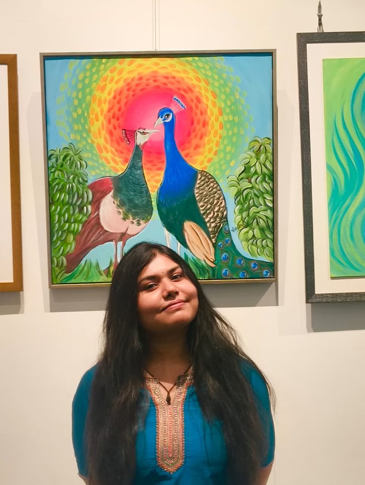 Vishakha standing beneath her framed peacock painting at an exhibition