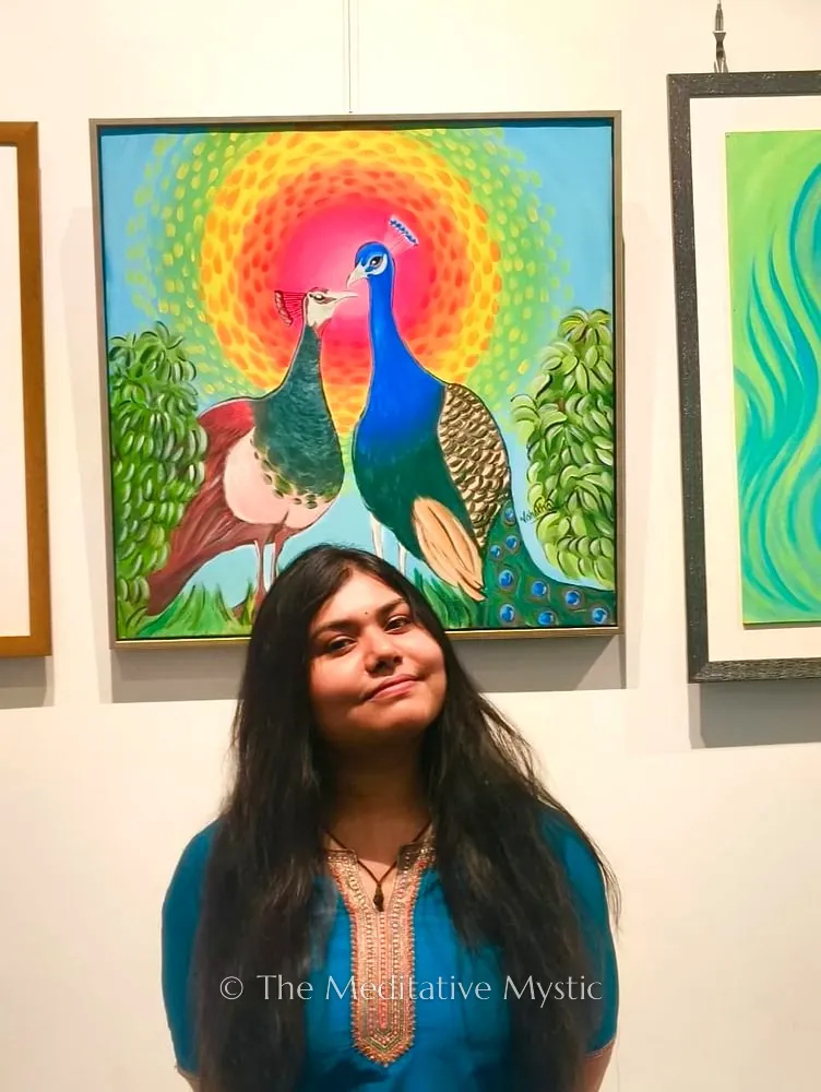 Vishakha Gautam standing in front of her peacock painting at an exhibition