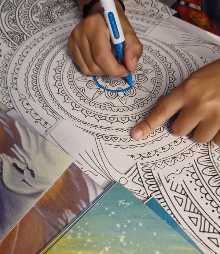 A hand colouring a detailed mandala with a blue pen during a session
