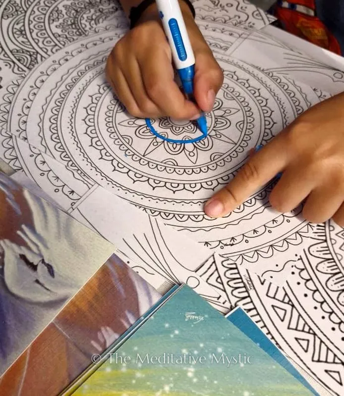 A hand colouring a detailed mandala with a blue pen during a session